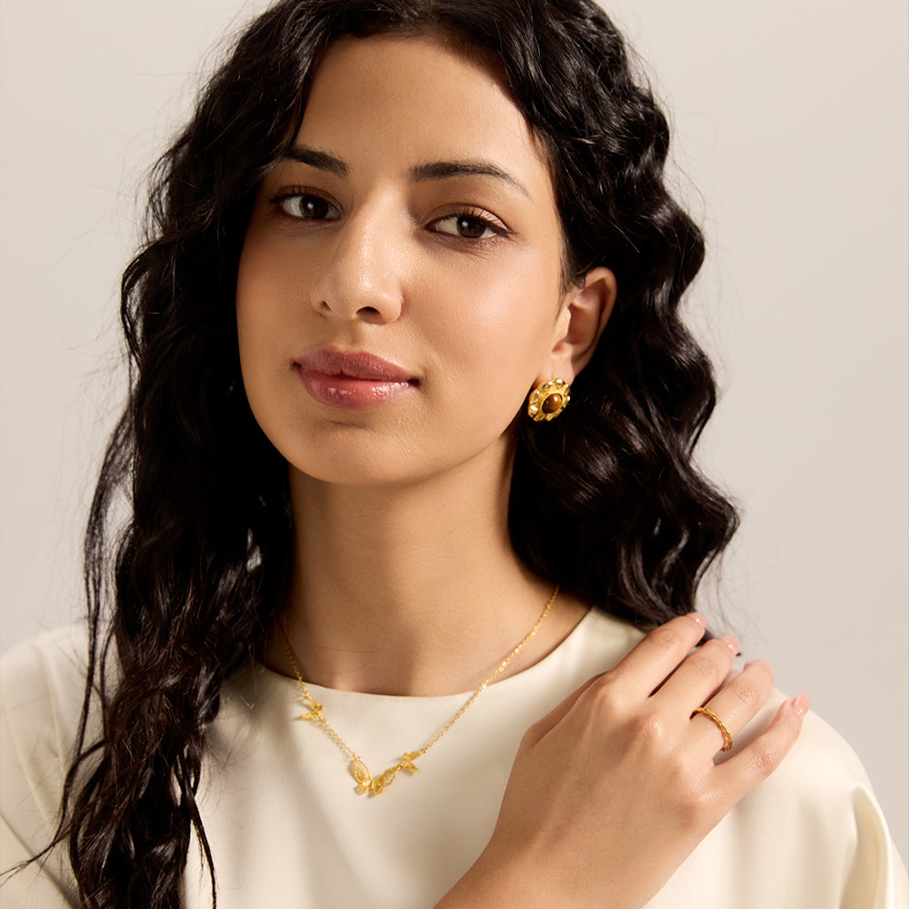 Model wearing Aveera designer gold plated flower tiger eye stud earrings, with matching necklace and ring, completing a chic look.