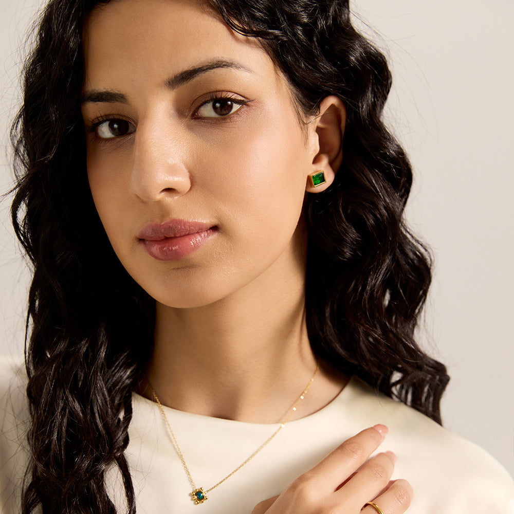Model wearing Aveera designer gold plated emerald green square stud earrings, with matching necklace, completing a chic look.