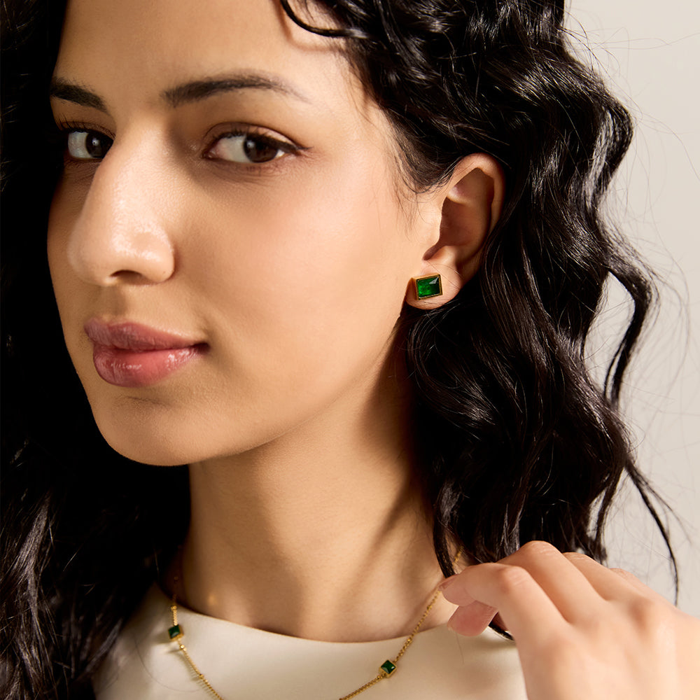 Close-up of model wearing Aveera designer gold plated emerald green square stud earring, highlighting vibrant green gemstone.