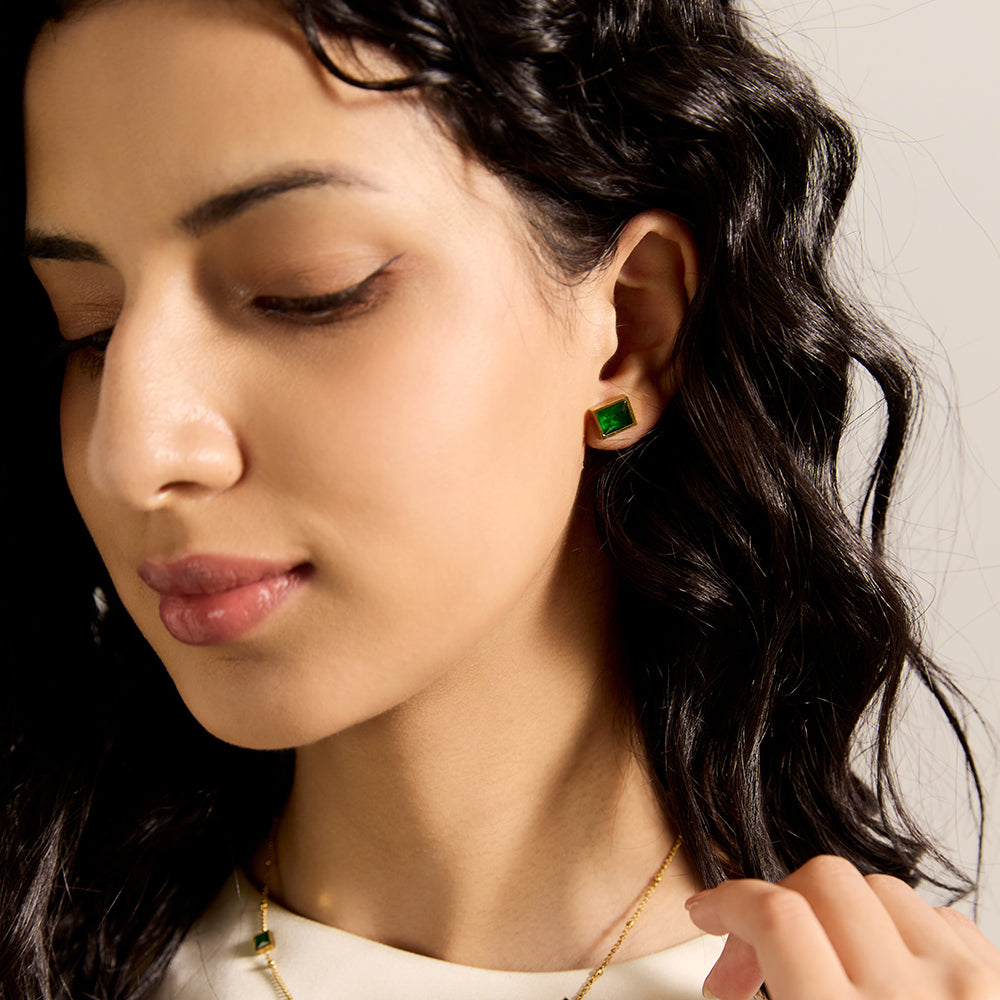 Close-up of model wearing Aveera designer gold plated emerald green square stud earring, highlighting vibrant green gemstone.