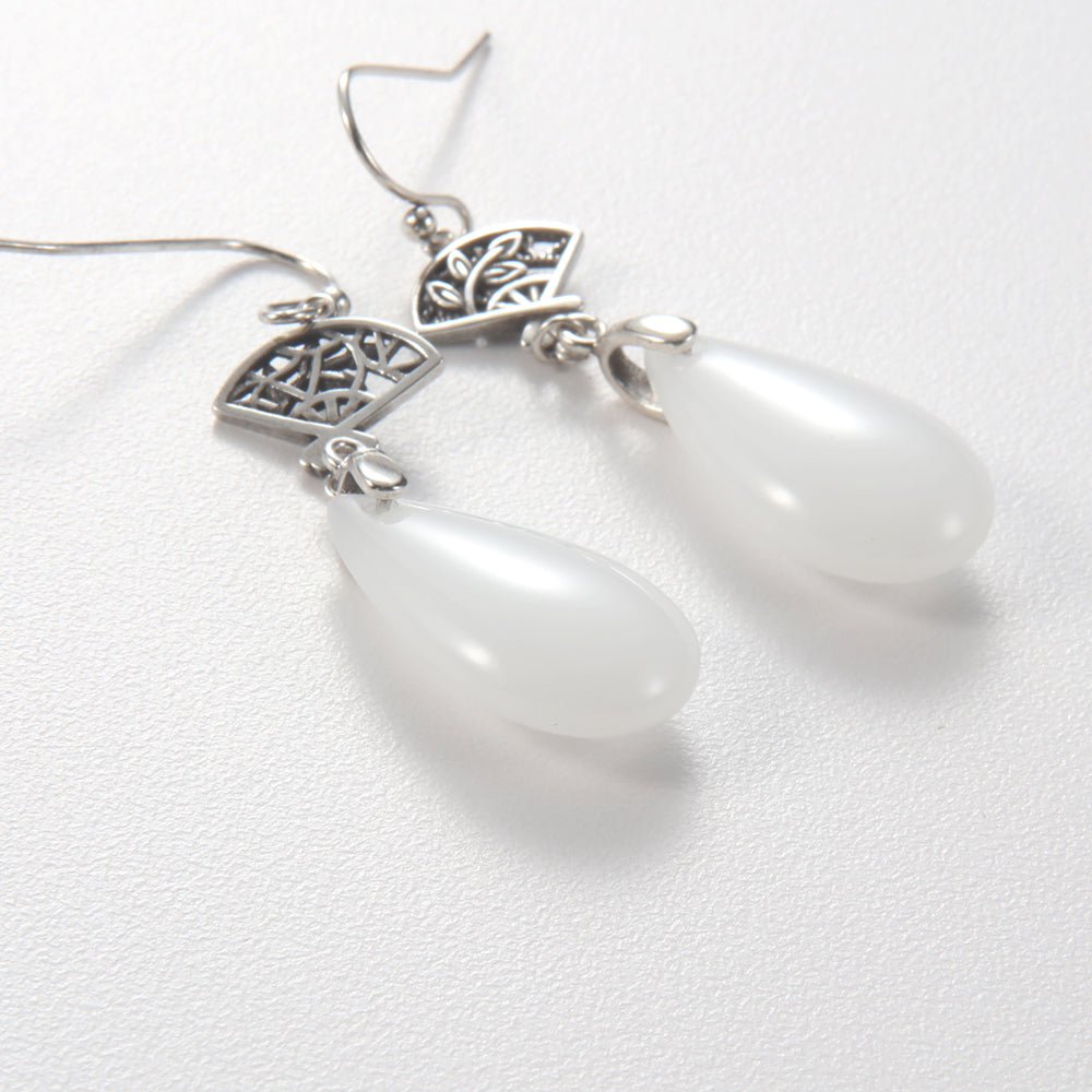 Close-up of Aveera designer filigree fan earring showing intricate silver-tone detail and luminous white teardrop pendant.