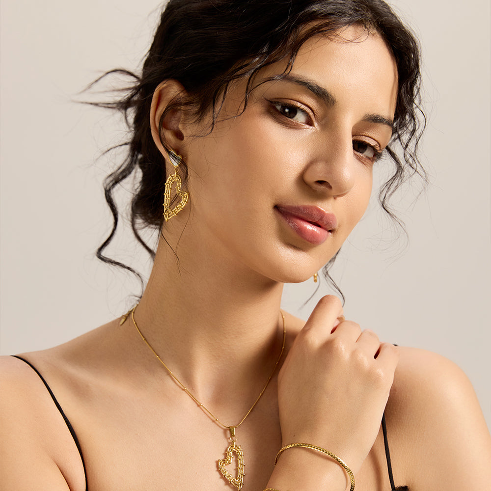 Model wearing Aveera designer gold plated hollow heart earrings, with matching necklace and bracelet, completing a chic look.