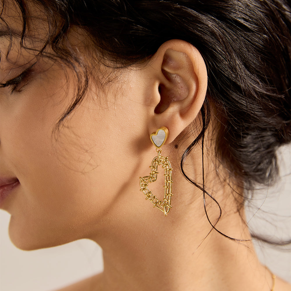Close-up of model wearing Aveera designer gold plated hollow heart mother of pearl drop earring, showcasing modern romantic style.