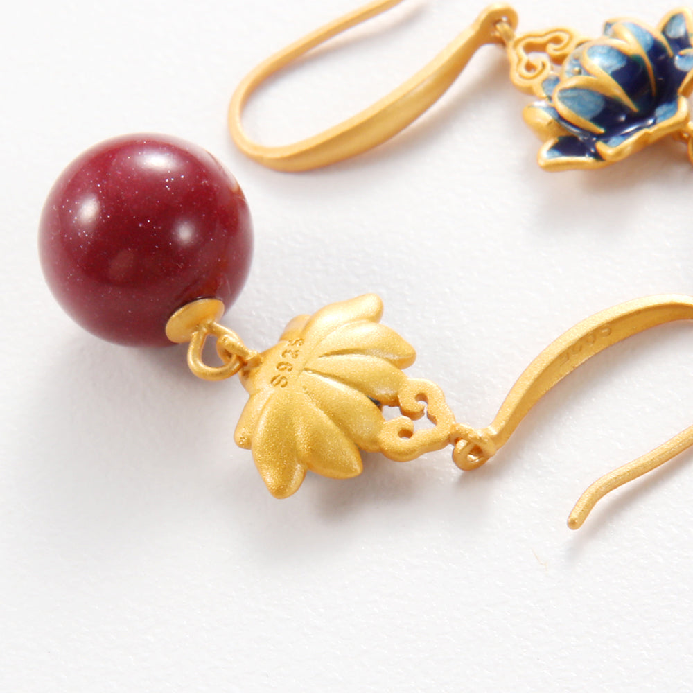 Close-up of Aveera designer drop earring showing intricate lotus detail, red orb, and S925 sterling silver hook for hypoallergenic wear.