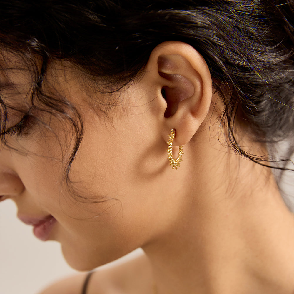 Model wearing Aveera designer gold plated sunburst textured half hoop earring, showcasing unique design.