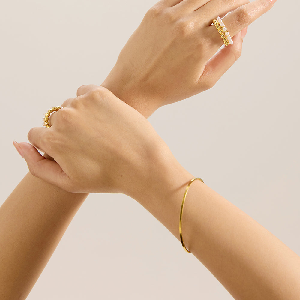 Model wearing Aveera gold tone minimalist closed bangle bracelet on wrist, showcasing its comfortable fit and simple elegance.