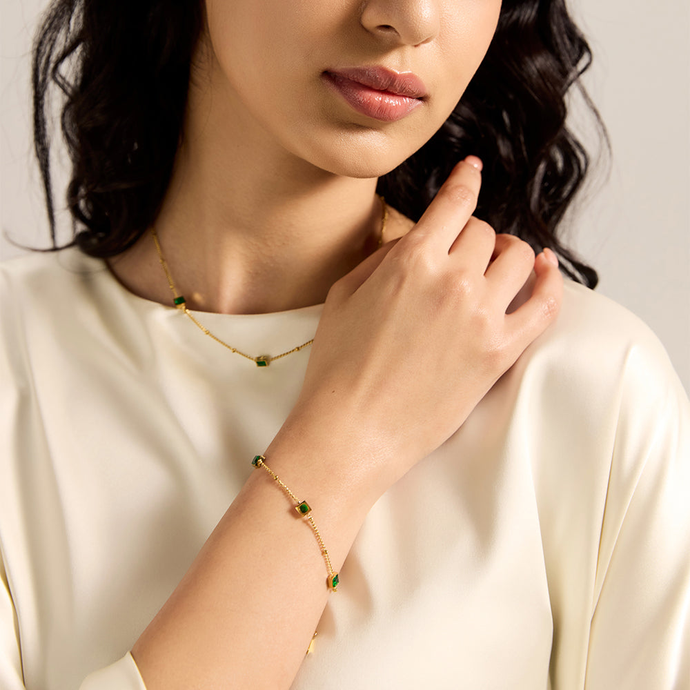 Model showcasing Aveera gold tone square green gemstone bracelet as part of an elegant outfit, highlighting its versatile appeal.
