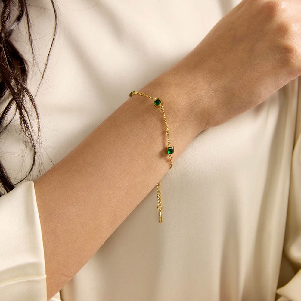 Close-up of Aveera gold tone square green gemstone bracelet on wrist, showing its delicate chain and vibrant stones.