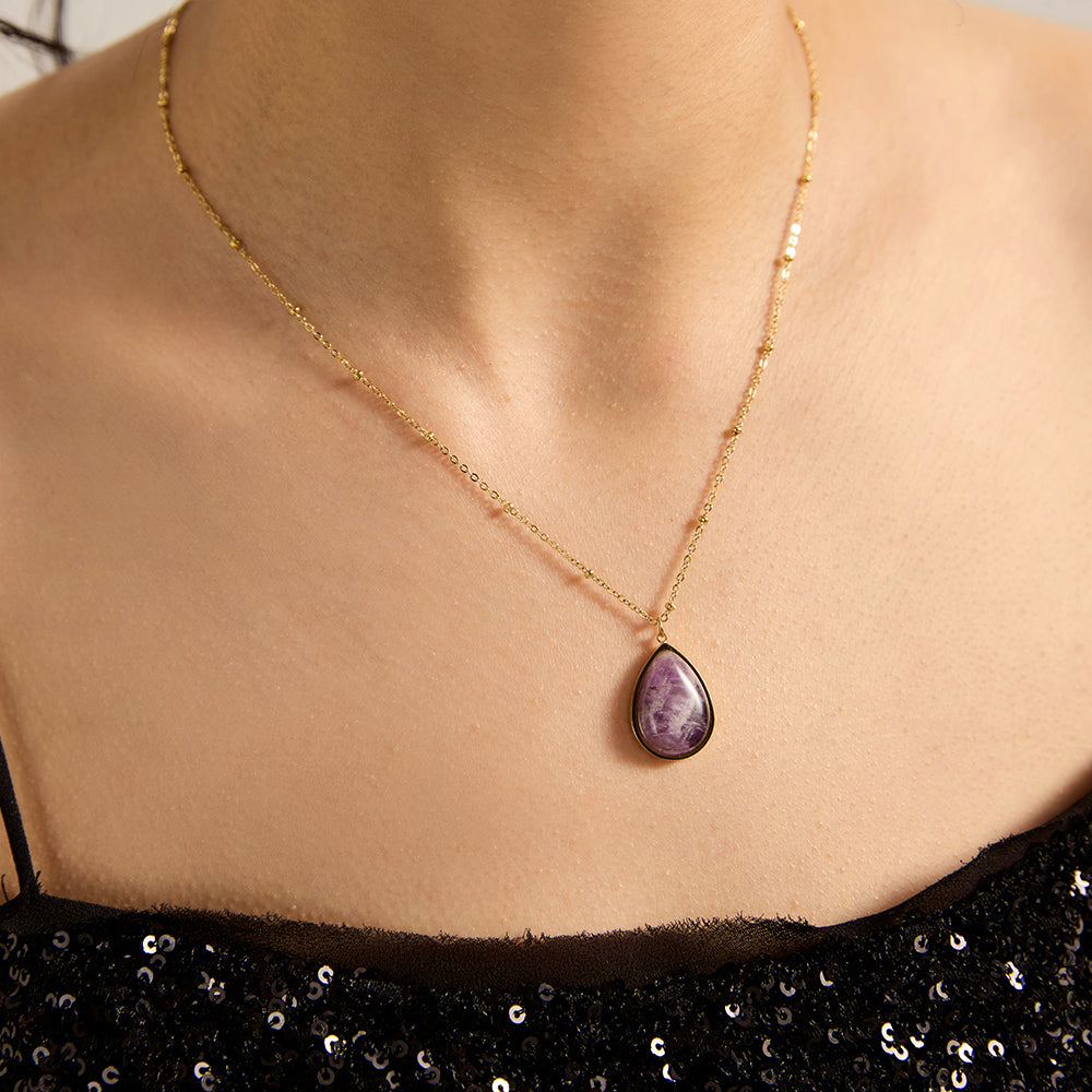 Woman wearing gold tone teardrop amethyst necklace, close-up showing the beautiful purple crystal and its calming presence on the neckline.