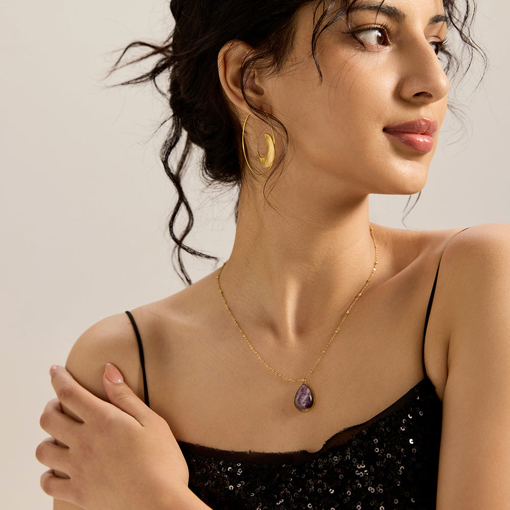  Woman modeling gold tone amethyst teardrop pendant necklace, showcasing its elegant spiritual appeal and how it enhances overall look.