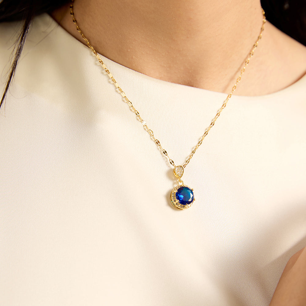 Woman wearing gold tone blue sapphire disc necklace, close-up highlighting the luminous blue gemstone and its wisdom-enhancing presence on the neckline.