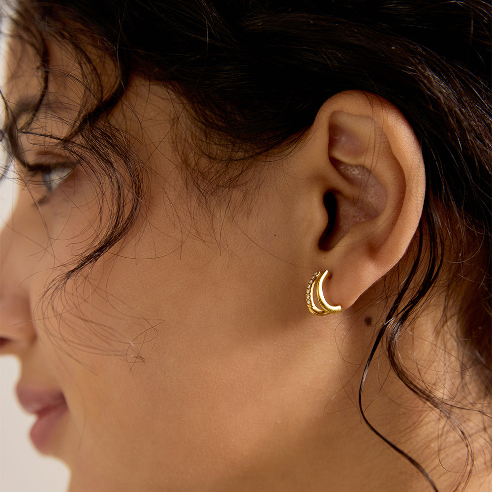 Close-up of woman wearing a single gold tone C-shaped micro pave stud earring, showing texture and sparkle.