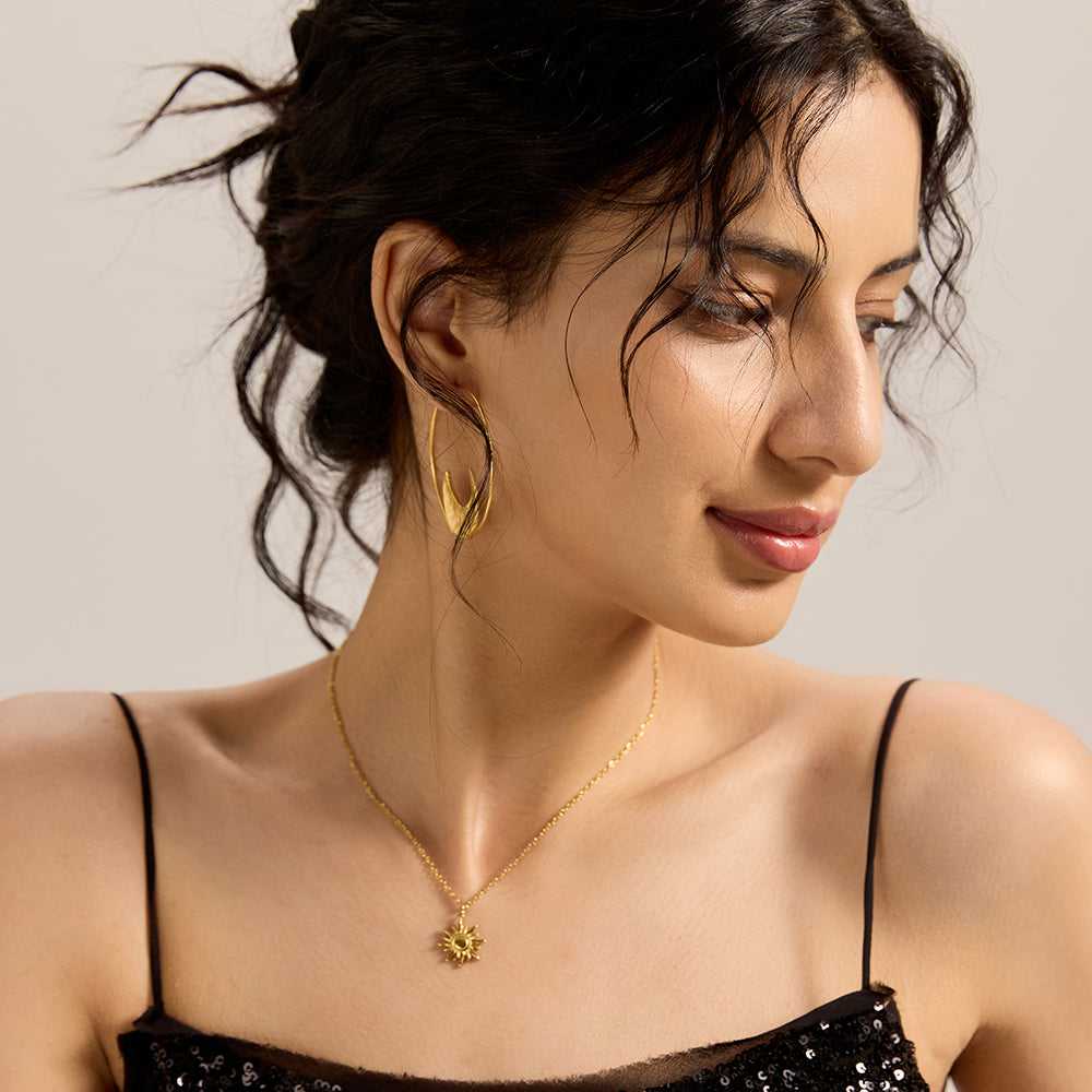 Woman wearing gold celestial sun and moon asymmetrical hoop earrings, showcasing full style.