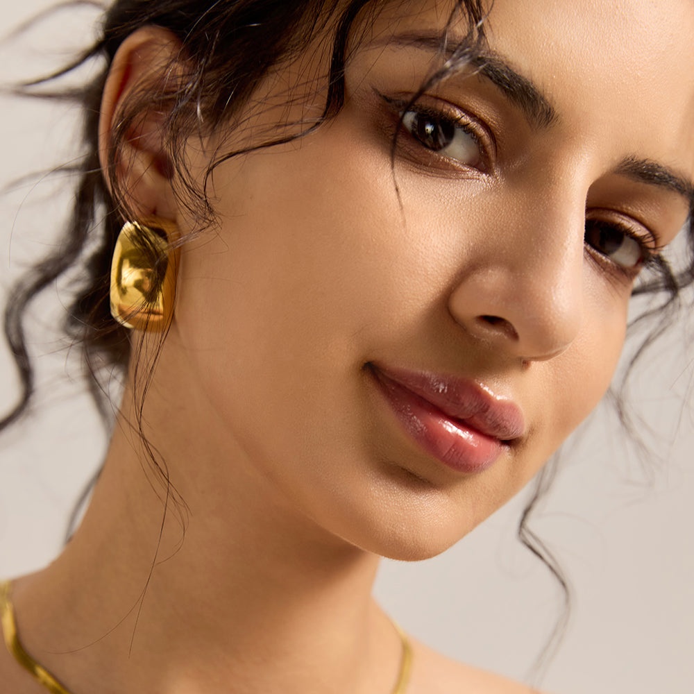 Close-up of woman wearing a single gold chunky dome hoop earring, highlighting the polished finish.
