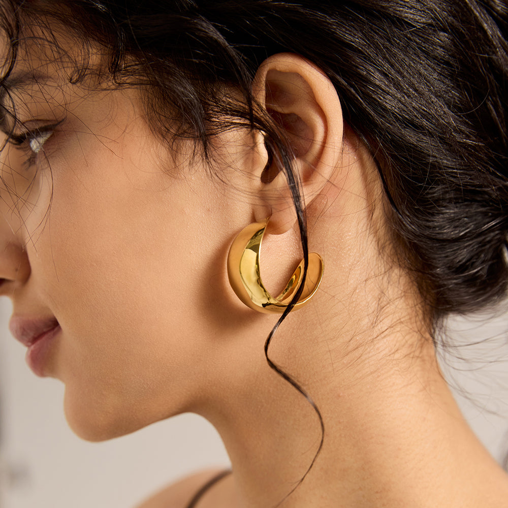 Side view of woman wearing bold gold dome hoop earrings, showing their size and form.