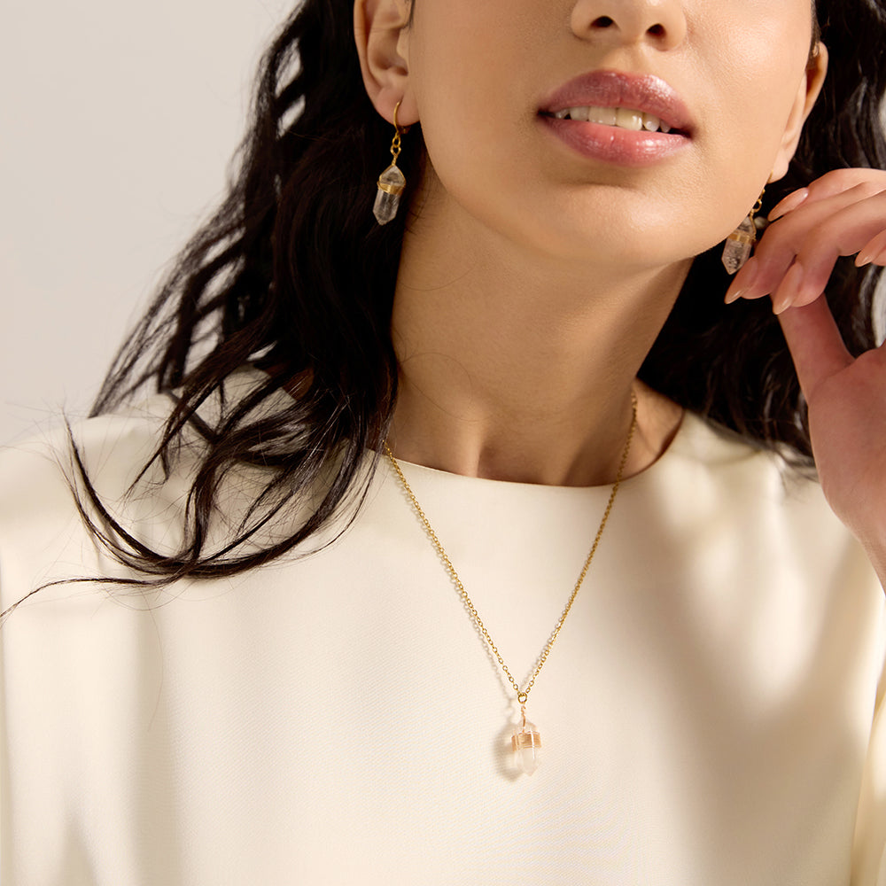 Woman wearing gold tone clear quartz crystal point necklace, close-up highlighting its transparent beauty and energy-directing shape on the neckline.