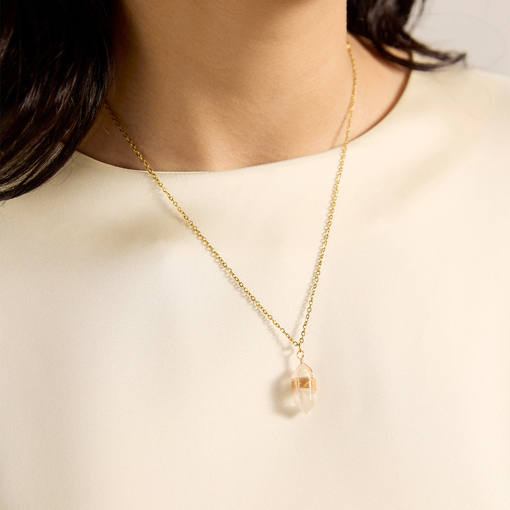 Woman wearing gold tone clear quartz crystal point necklace, close-up highlighting its transparent beauty and energy-directing shape on the neckline.