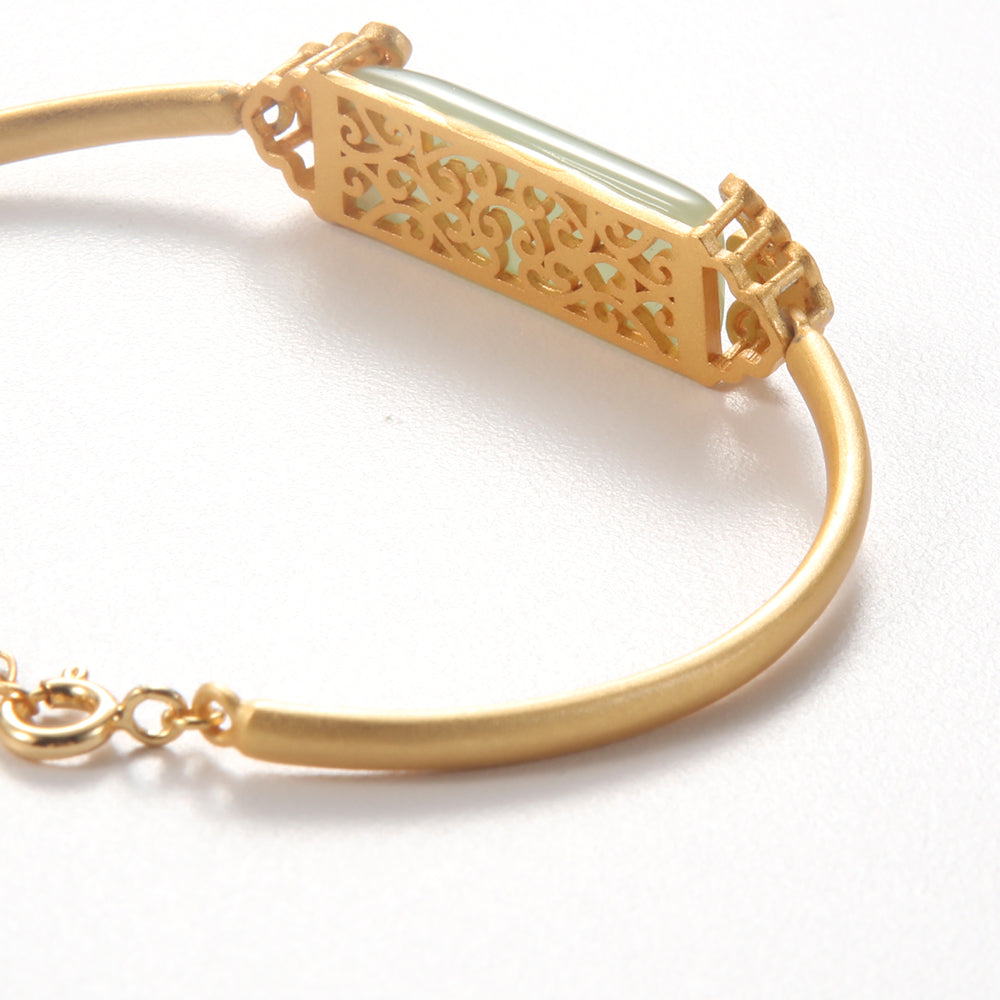 Close-up of woman's wrist wearing vintage gold bangle with green gemstone and pearl details.