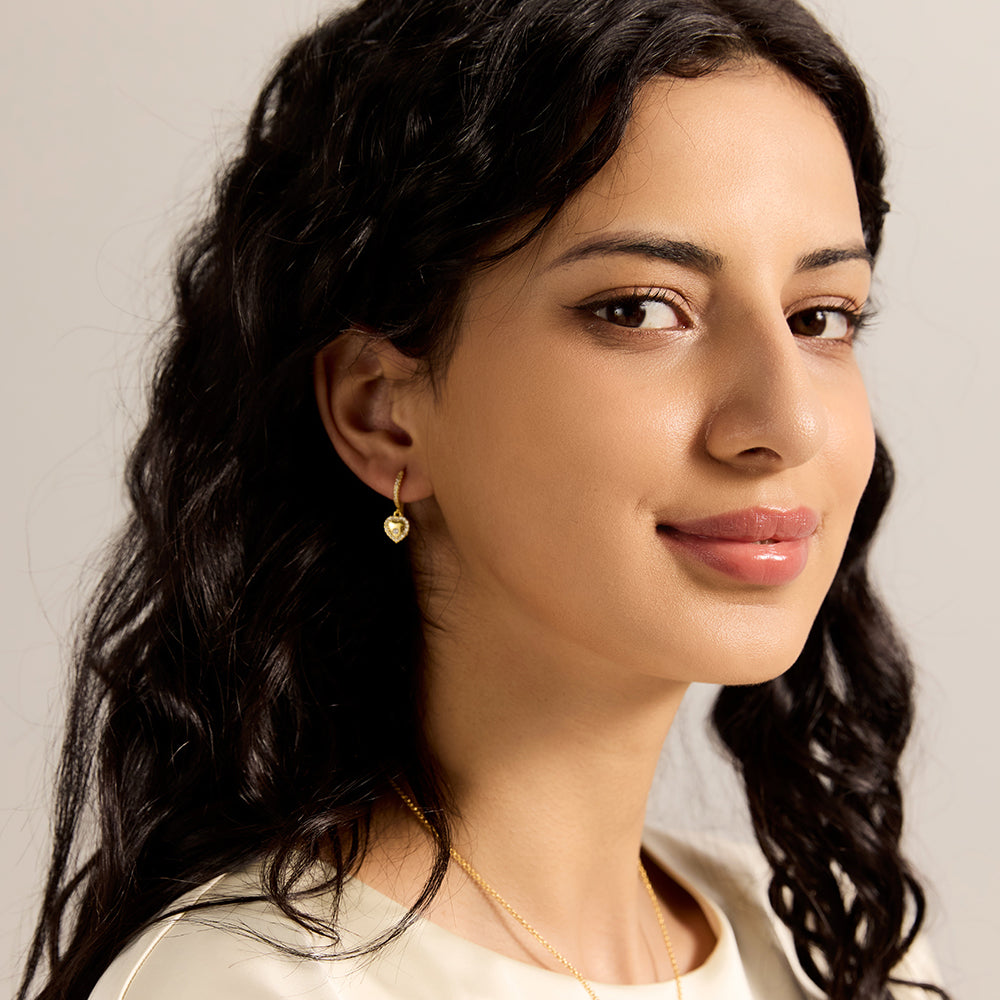 Side view of woman wearing elegant gold heart dangle hoop earrings for everyday style.