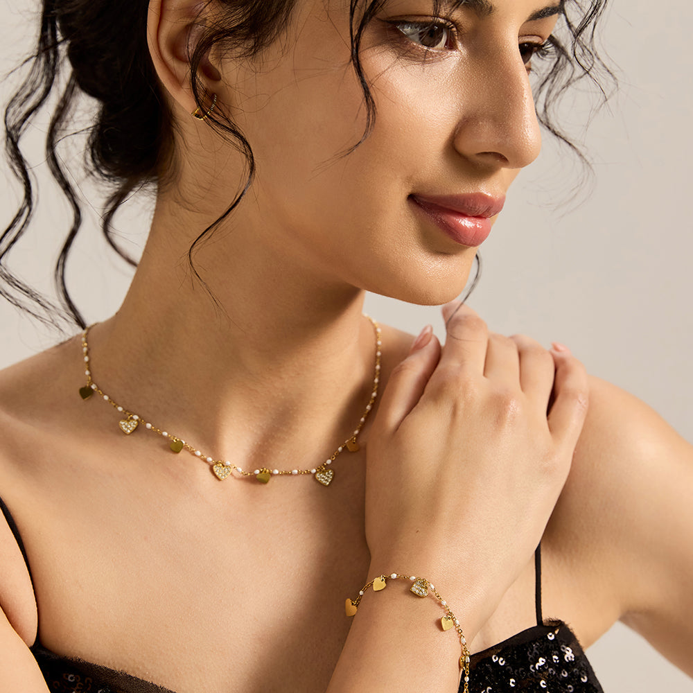 Woman wearing elegant gold tone heart charm bracelet with pearl accents.