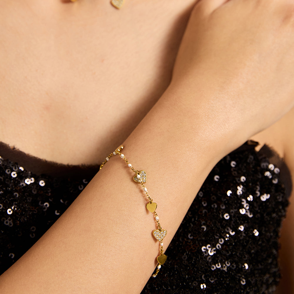 Woman with gold heart charm necklace and matching bracelet with pearls.