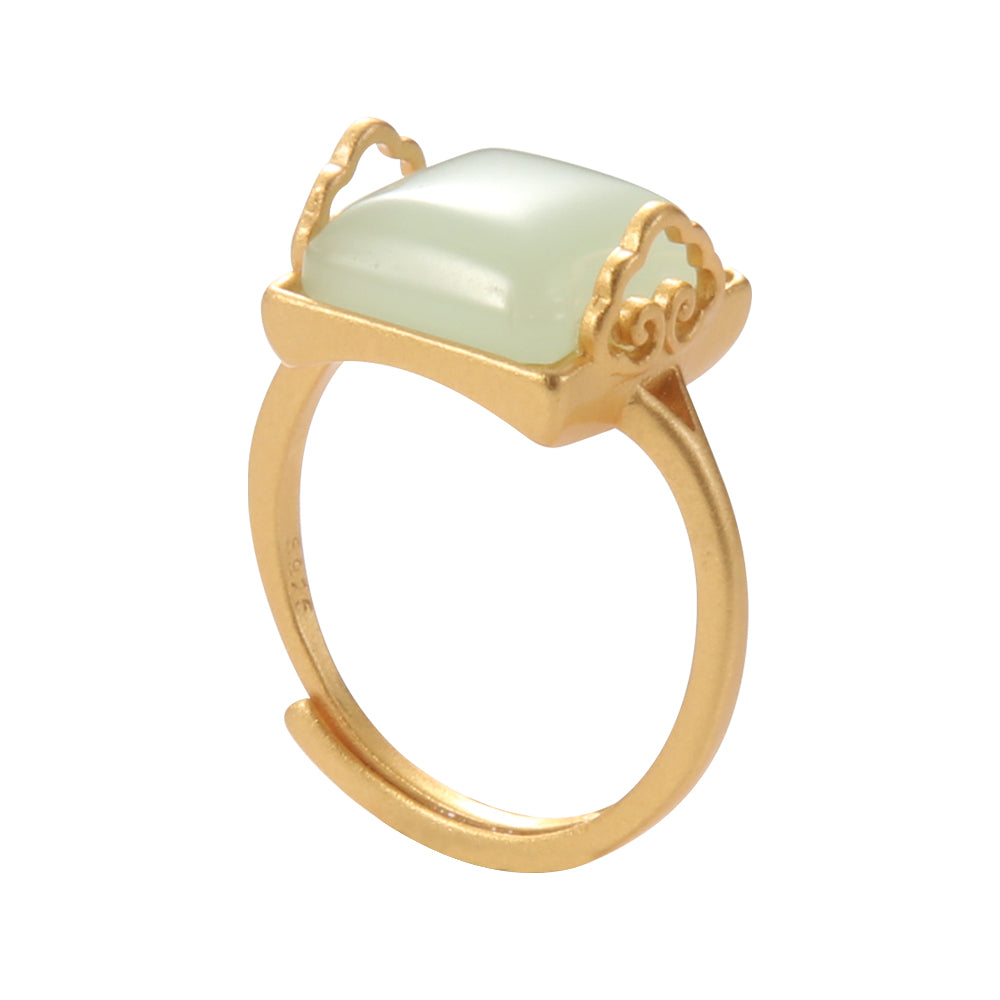 Close-up of gold tone natural jade or light green stone ring, showcasing the square gemstone and decorative band details, representing ancient wisdom.