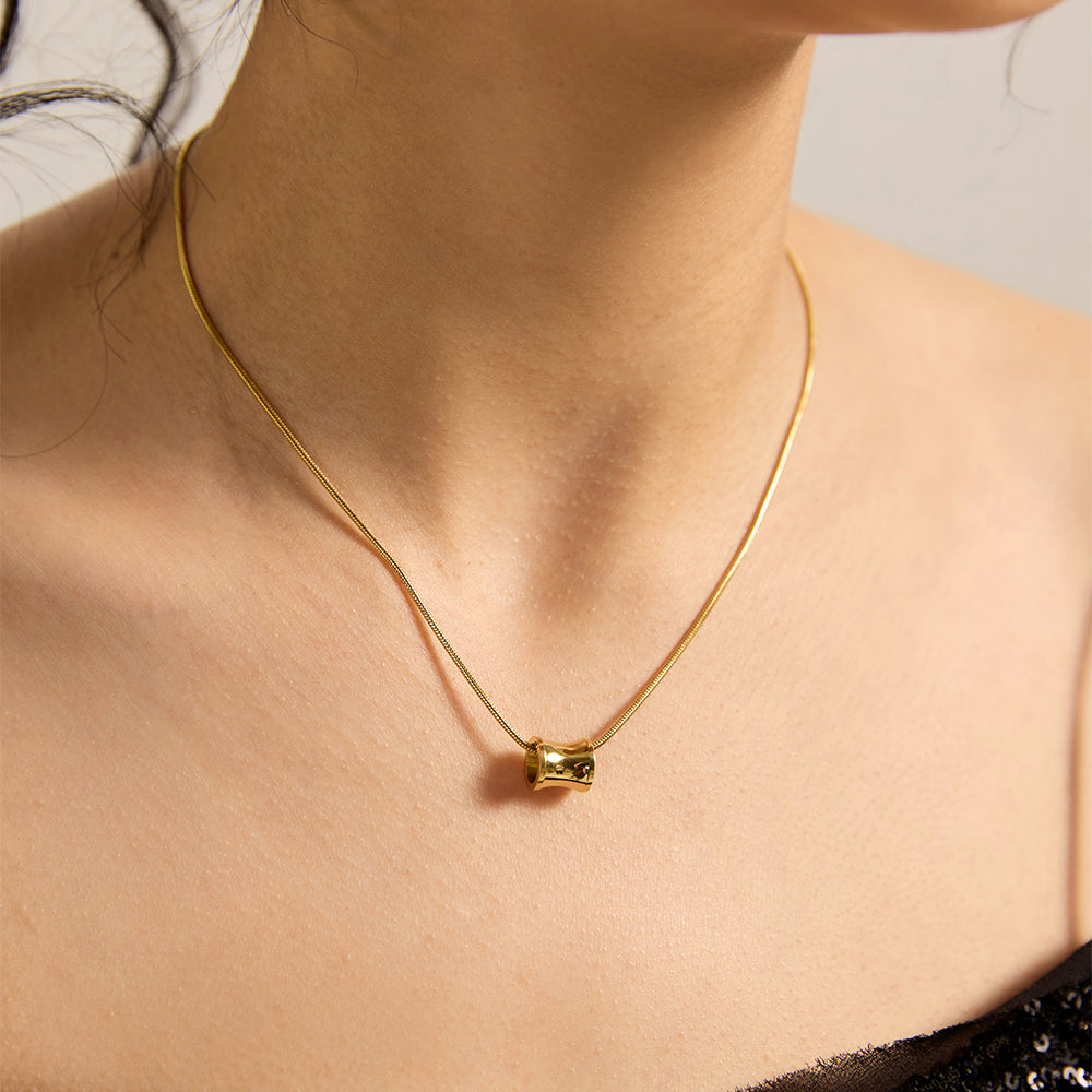 Woman wearing gold tone minimalist tube energy necklace, close-up highlighting its sleek design and subtle power on the neckline.