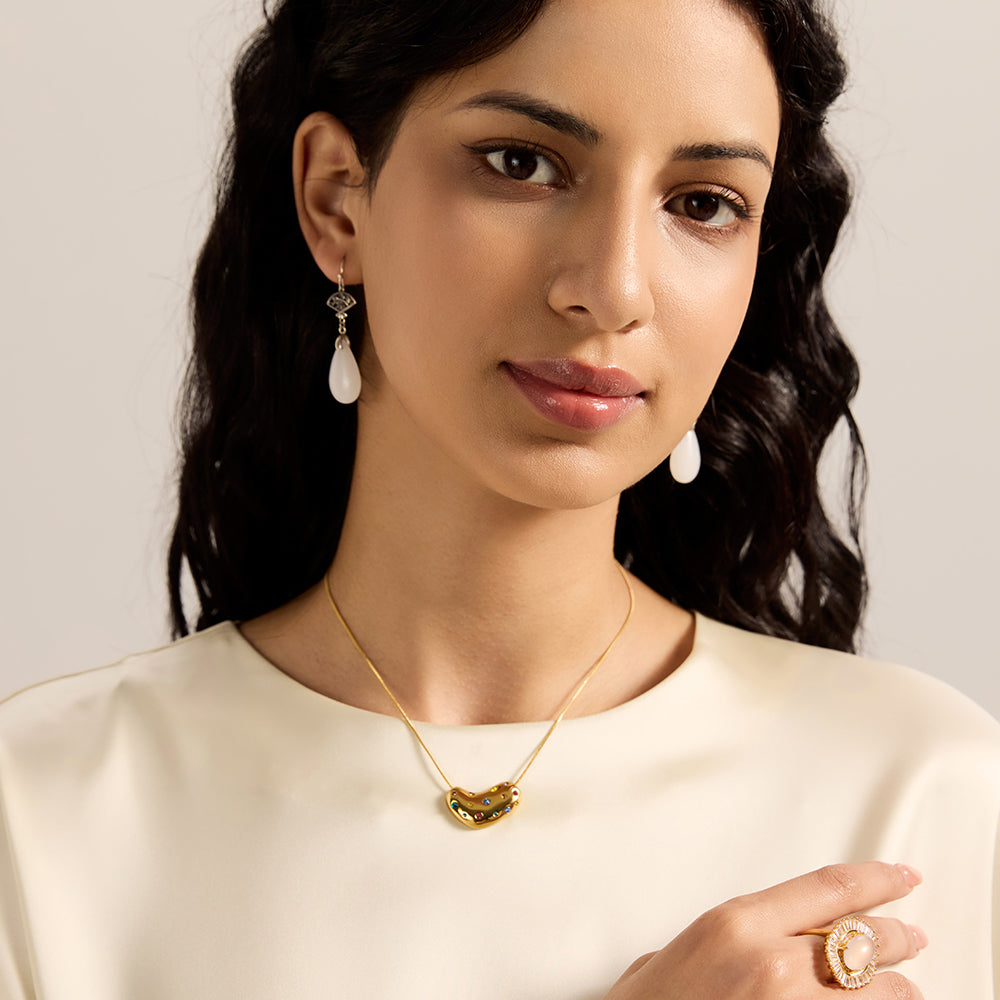 Woman modeling gold tone bean necklace with colorful crystals, highlighting its vibrant appeal and how it sits on the neckline.