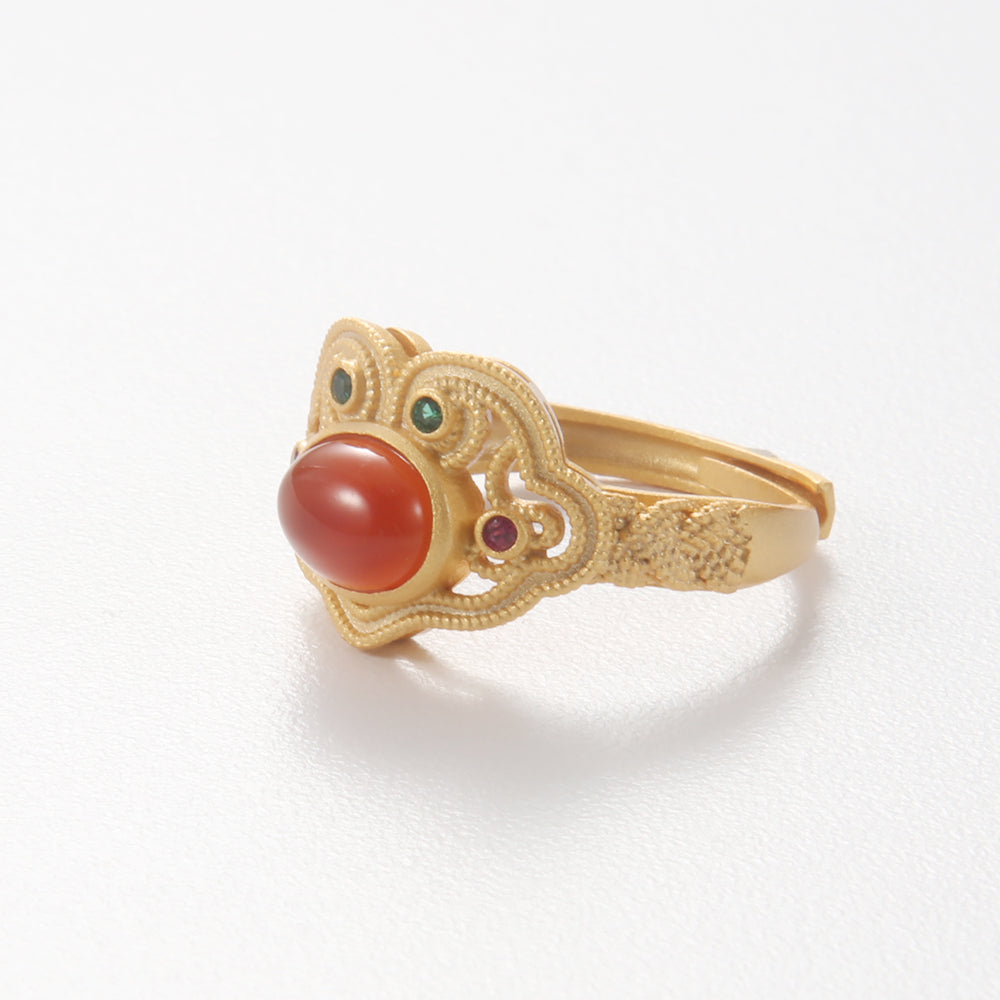 Gold tone ornate ring with a prominent oval red-orange Carnelian or Red Jasper cabochon stone, symbolizing vitality and protection.