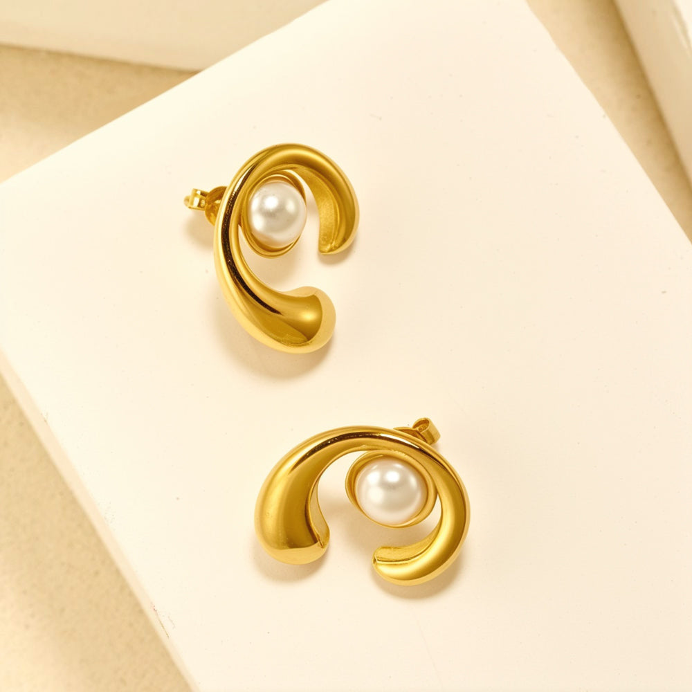 Pair of gold tone sculptural stud earrings with a white pearl nestled in a modern swirl design on white background.