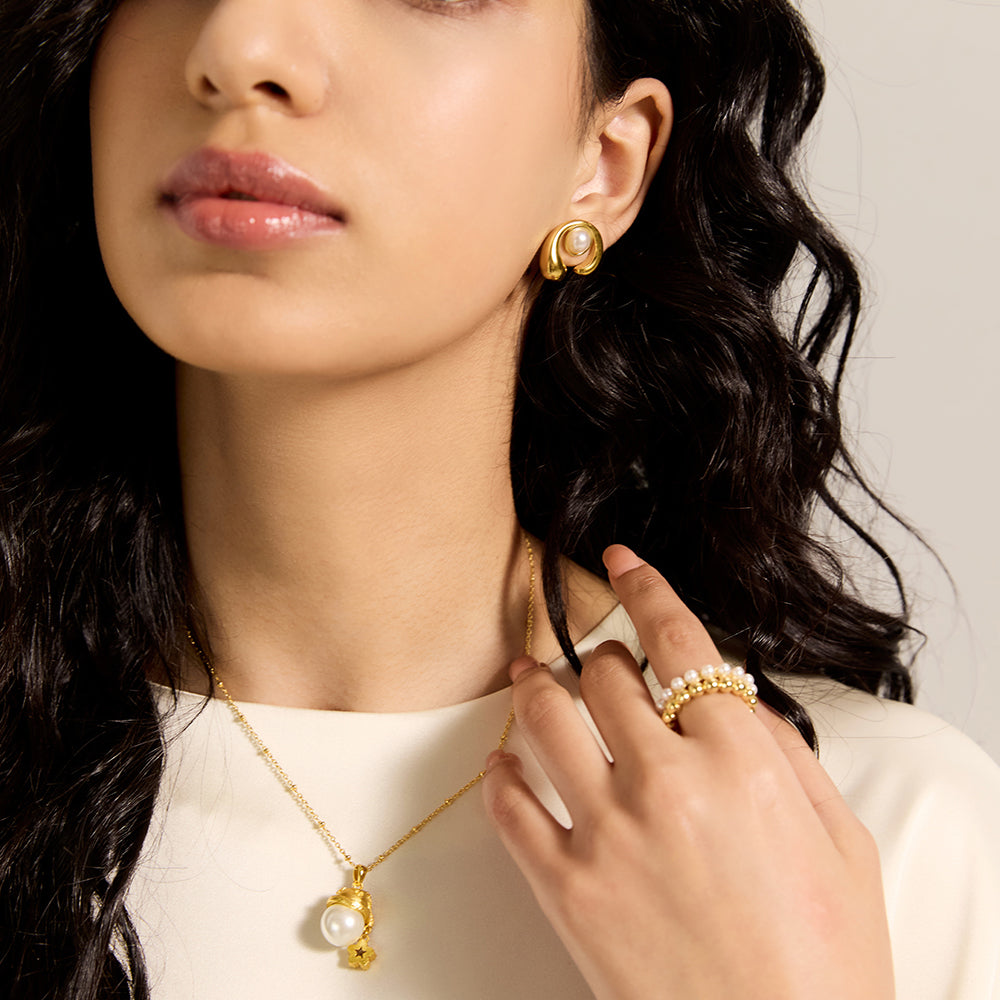 Close-up of gold tone sculptural pearl stud earrings, highlighting the unique swirl design and pearl luster.