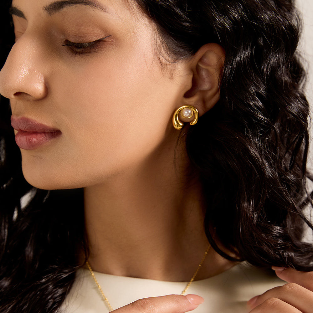 Close-up of woman's ear wearing a gold tone sculptural pearl stud earring, showcasing the design worn.
