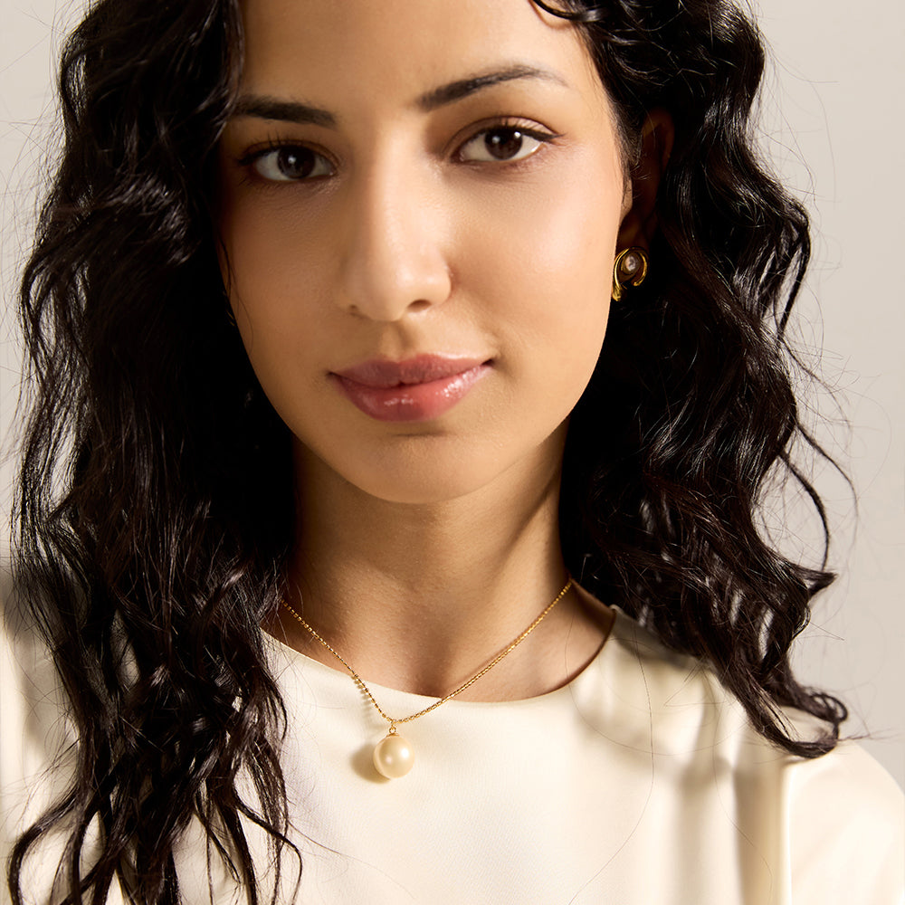  Woman wearing gold tone spherical pearl necklace, close-up highlighting the lustrous pearl and its elegant, pure presence on the neckline.