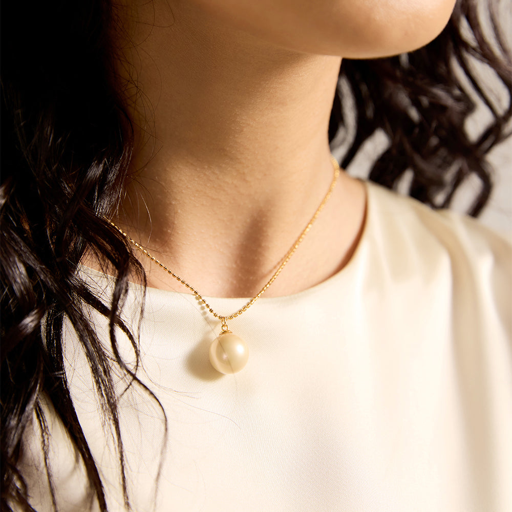 Woman modeling gold tone spherical pearl necklace, showcasing its timeless elegance and spiritual significance.