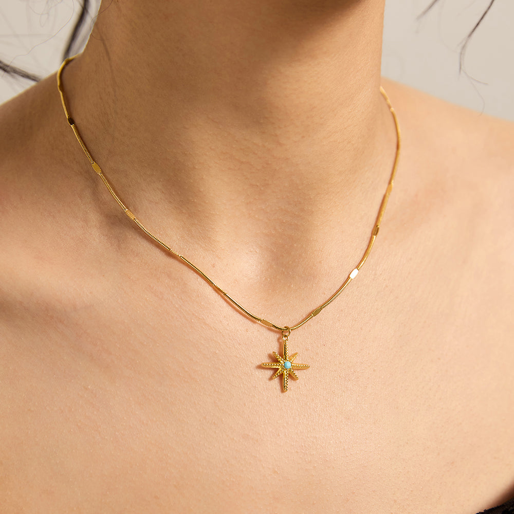Woman wearing a gold tone starburst pendant necklace with a turquoise accent, showing its delicate look on the neckline.