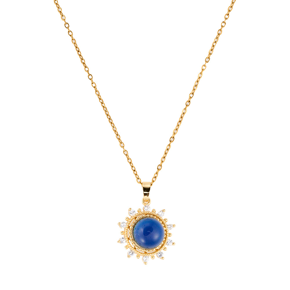 Radiant gold tone sunburst pendant necklace featuring a central blue gemstone, symbolizing wisdom, truth, and inner light, flat lay.