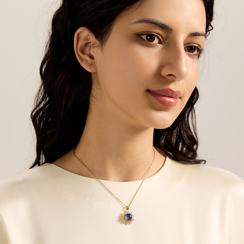Woman modeling gold tone sunburst necklace with a blue center stone, showcasing its elegant and spiritually uplifting presence.
