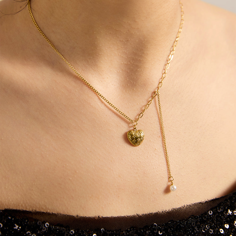 Close-up of model wearing gold tone textured heart necklace with pearl dangle.