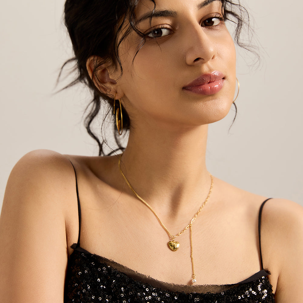 Model wearing gold tone textured heart and pearl dangle necklace, front view.