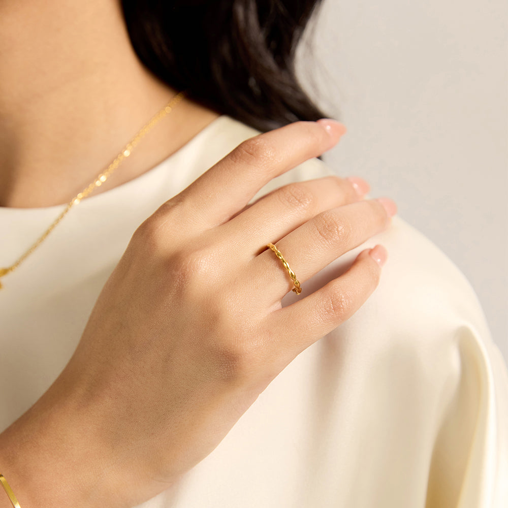 Close-up of a woman's hand wearing a gold tone textured twist band ring, showcasing its subtle detail.