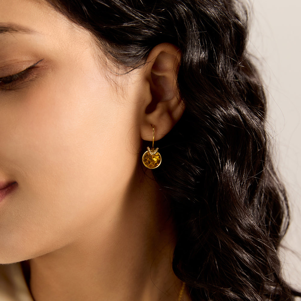 Woman wearing gold tone amber/yellow-brown gemstone stud earrings, highlighting overall look and elegance.