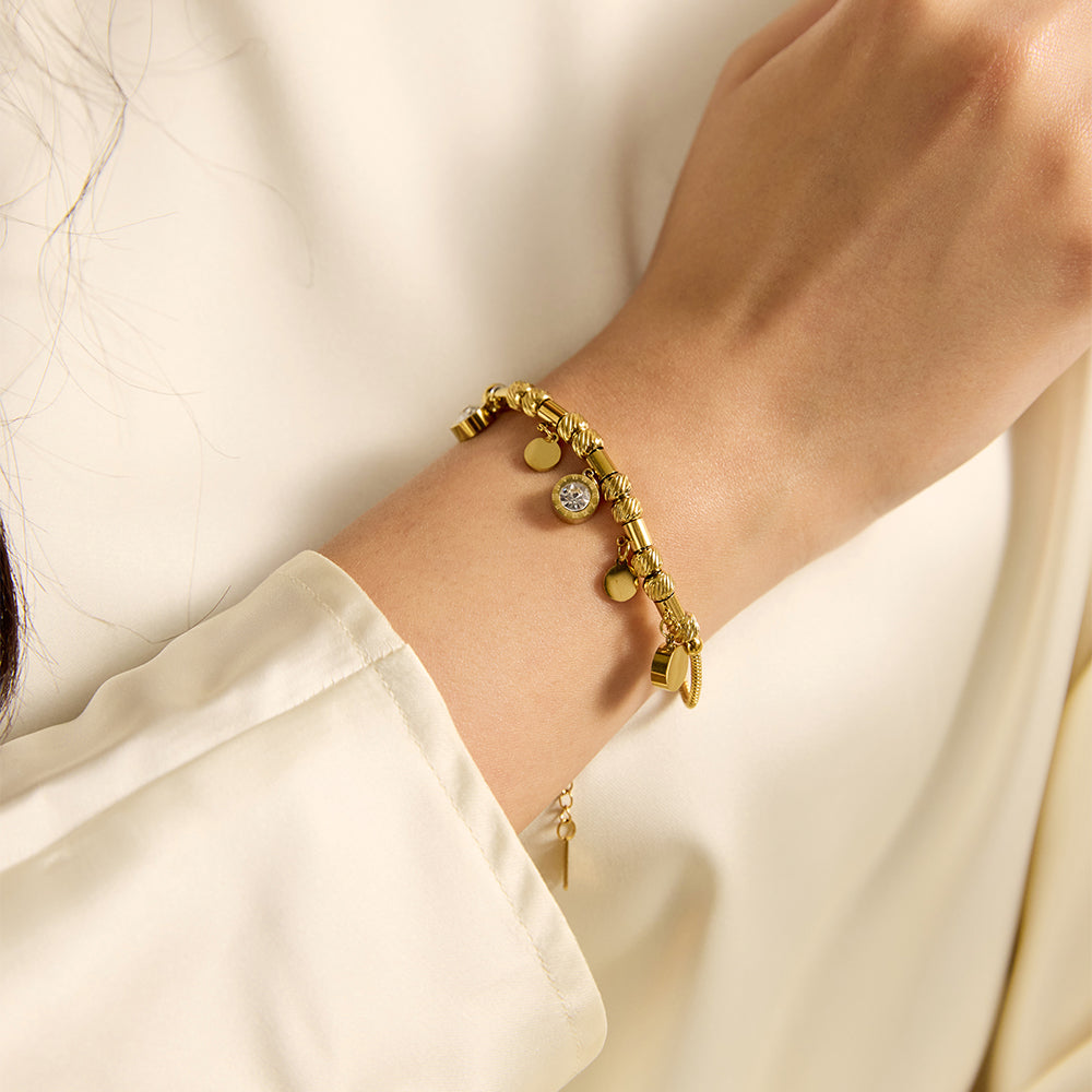 Woman wearing elegant gold tone barrel bead bracelet, close-up of charms.