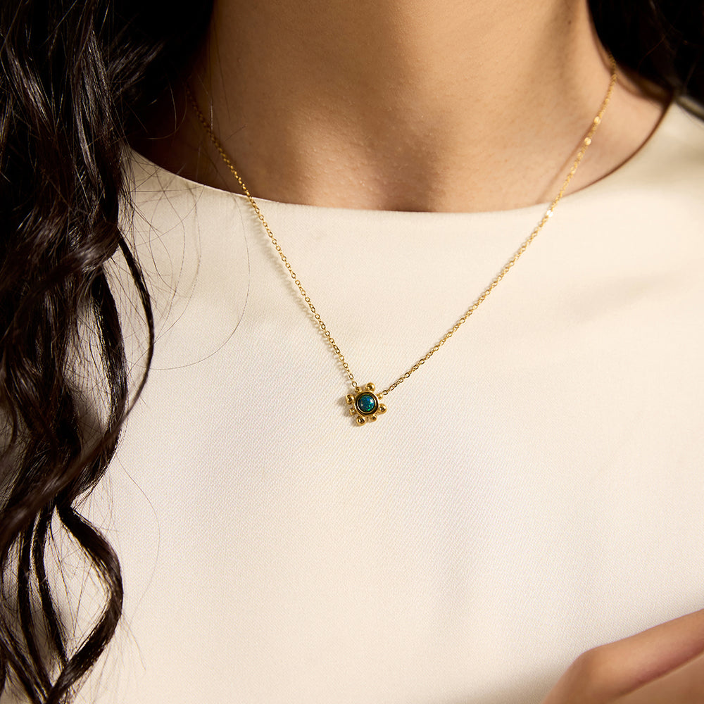 Woman wearing elegant gold tone green stone necklace, showing charm detail.