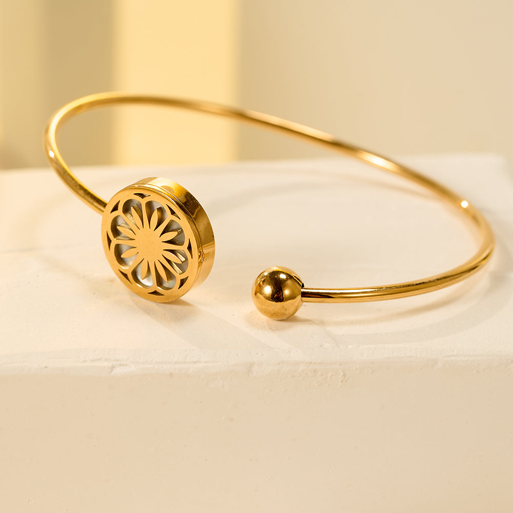 Chic gold tone open cuff bangle with a central floral motif.