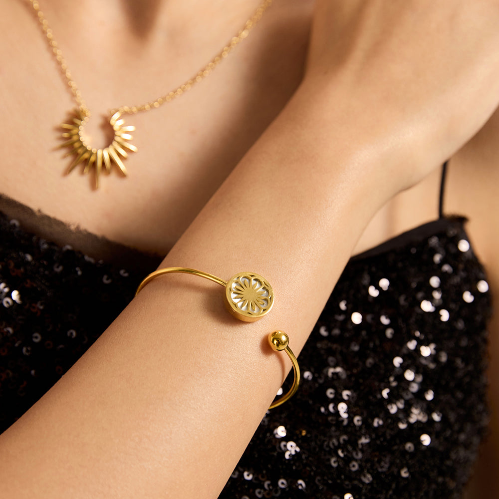 Woman wearing chic gold tone open cuff bangle with floral motif and matching necklace.