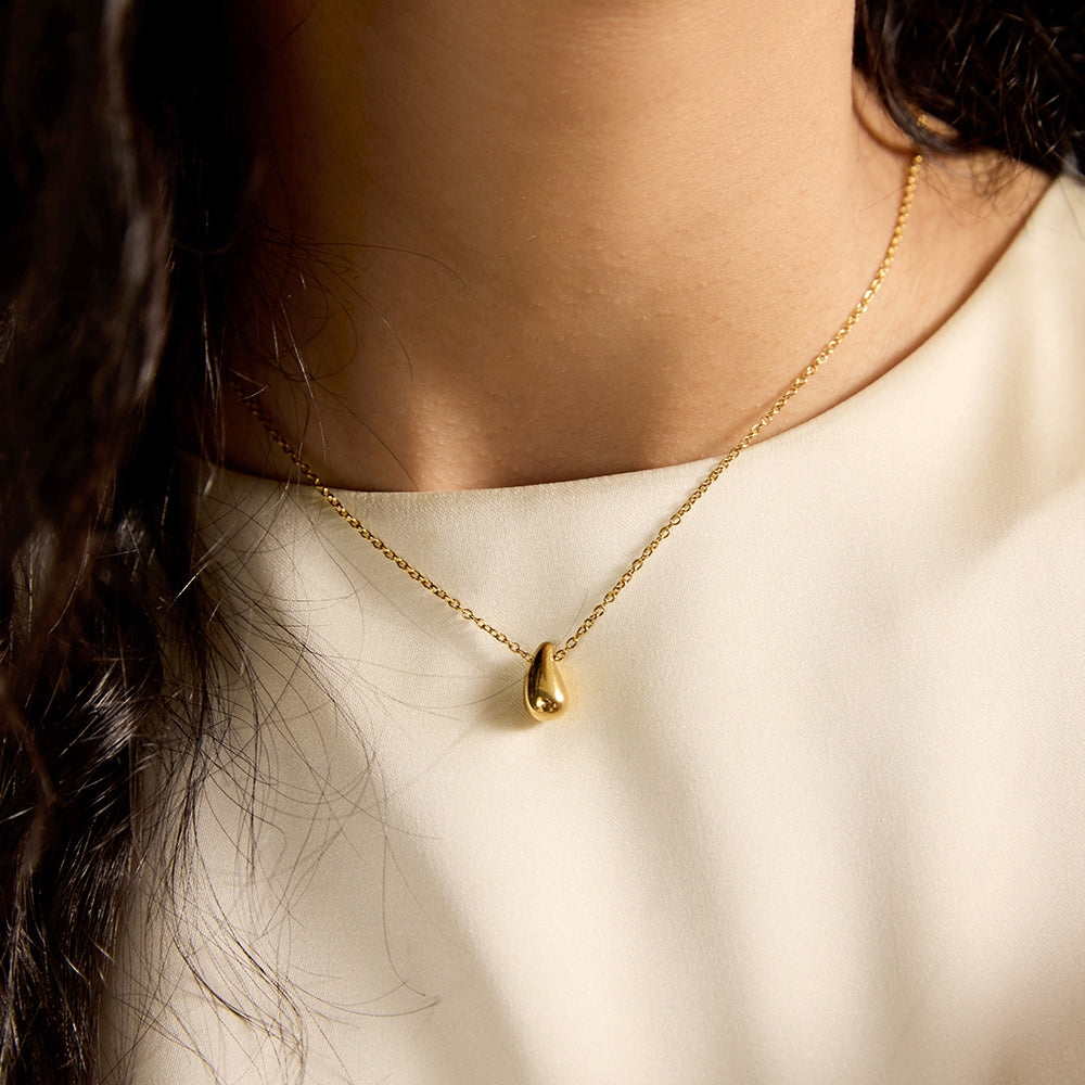 Woman wearing elegant gold tone tear-drop pendant necklace, close-up.