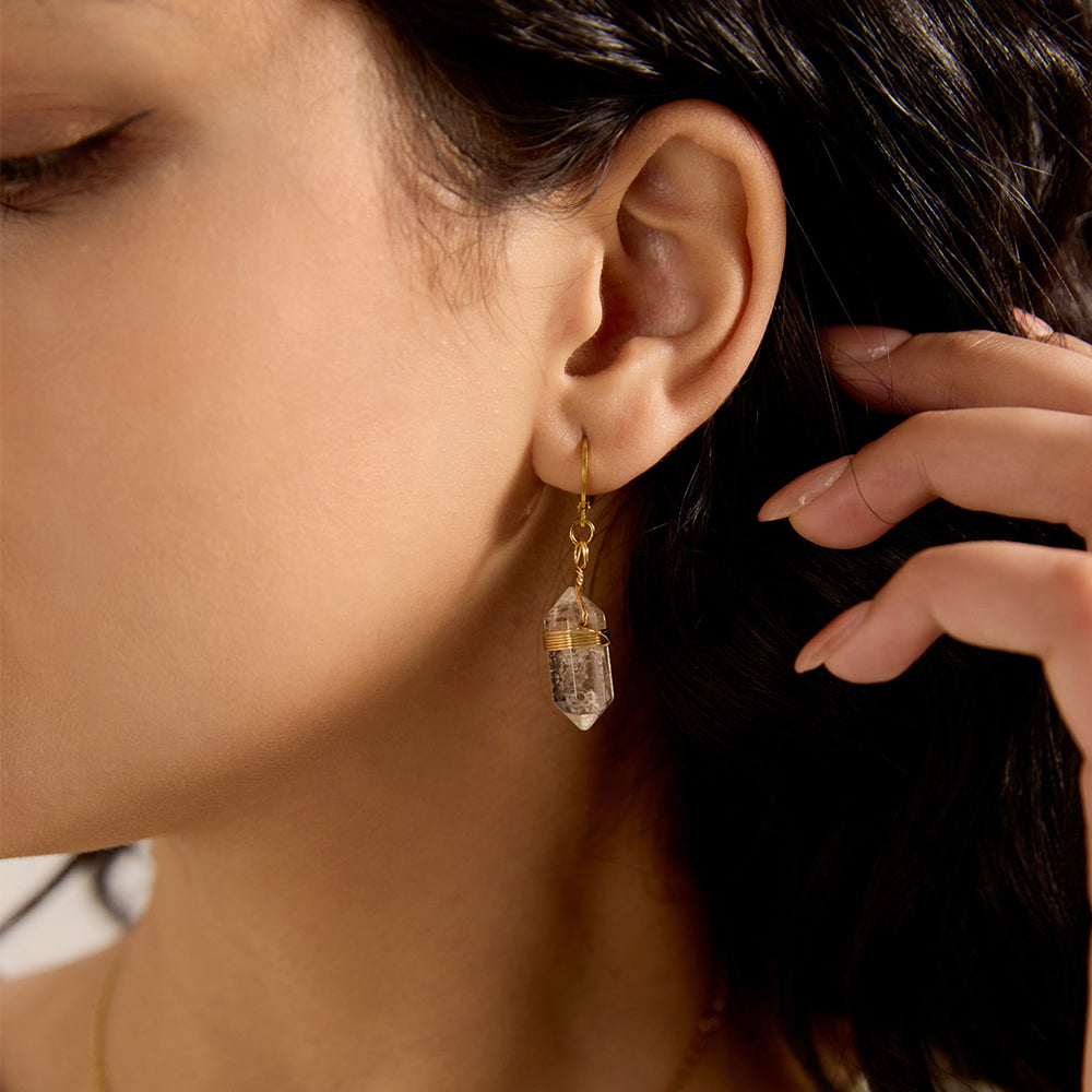 Close-up of woman's ear wearing a gold thin hoop earring with a wrapped natural crystal point dangle, reflecting spiritual energy.