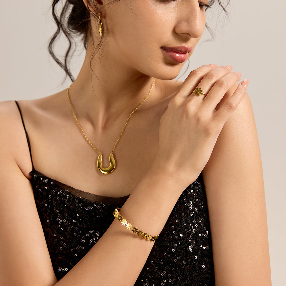 Model wearing gold daisy chain bracelet with matching gold necklace and ring, completing a chic evening look.