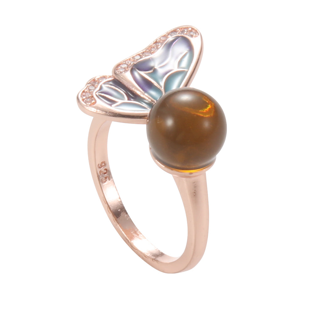 Rose gold tone open ring with a detailed butterfly motif and a round brown/amber grounding stone, symbolizing personal transformation.