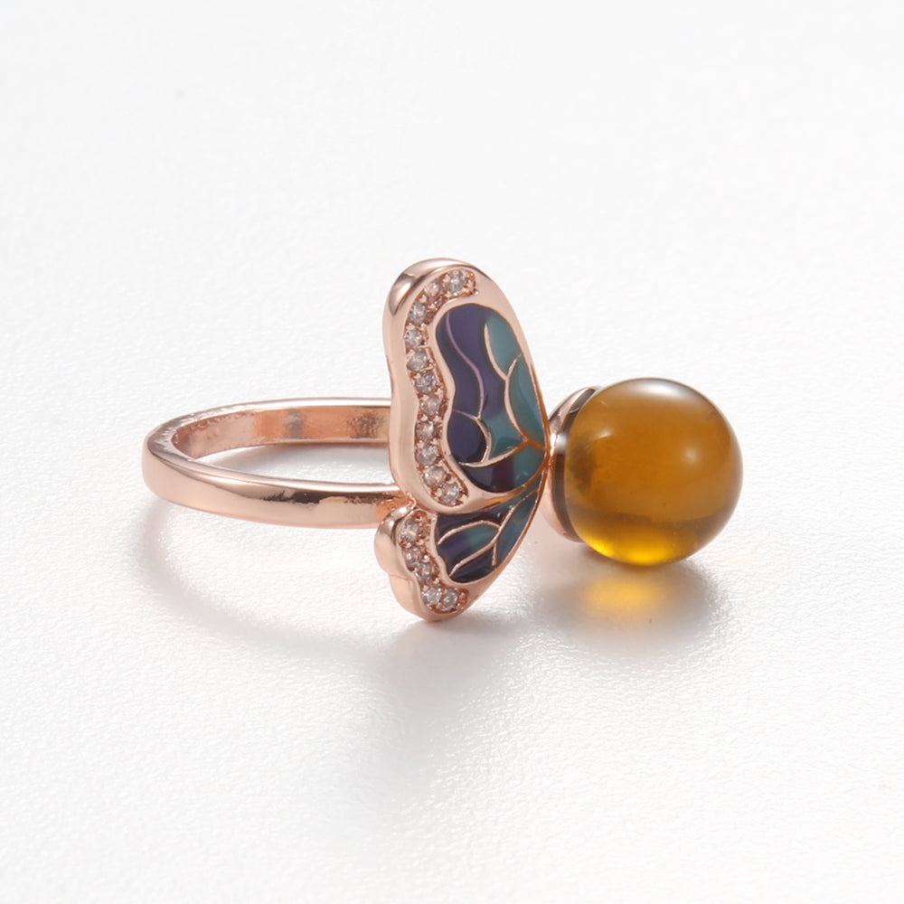 Close-up of a woman's hand wearing a rose gold butterfly ring with a natural earth-toned stone, representing spiritual growth and inner peace.
